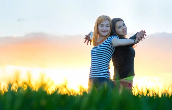 Дві молоді жінки обіймаються і відпочивають під час заходу сонця на відкритому повітрі. Найкращі друзі — стокове фото