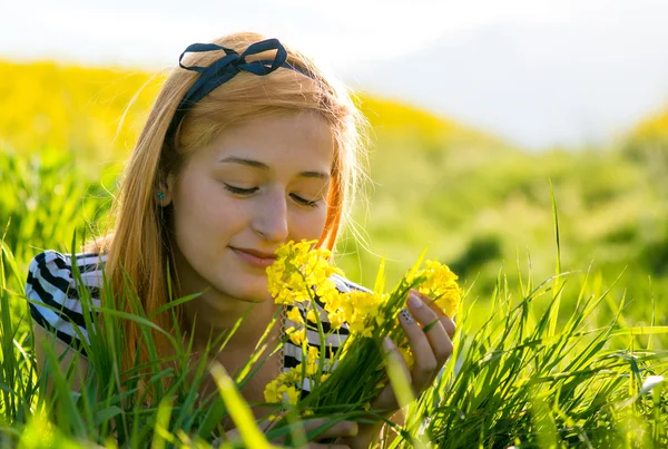 Portrait of beautiful young long-haired woman lying in park and smelling flowers — Stock Photo, Image