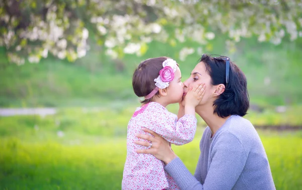 小さな女の子を抱いて、緑色の背景上の彼女の母親のキス — ストック写真