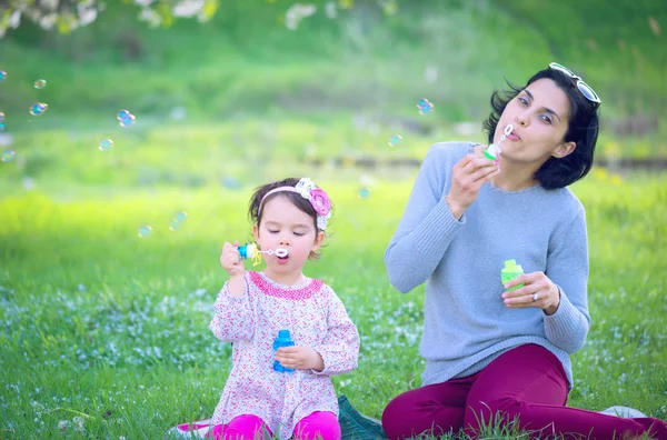 Gelukkig jonge moeder en haar dochter blazen van zeepbellen in park — Stockfoto