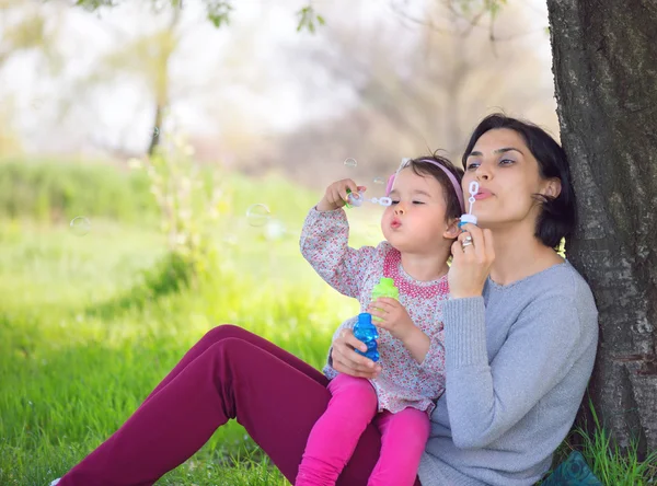 Glückliche junge Mutter und ihre Tochter pusten Seifenblasen im Park — Stockfoto