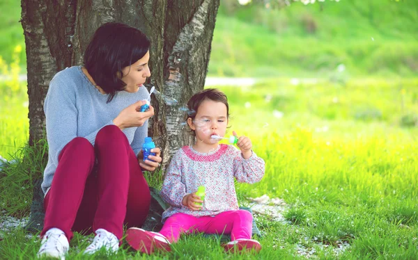 Gelukkig jonge moeder en haar dochter blazen van zeepbellen in park — Stockfoto