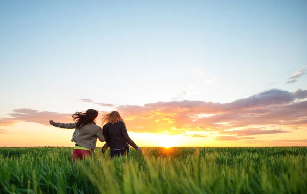 Duas amigas correndo em trigo para o pôr do sol — Fotografia de Stock