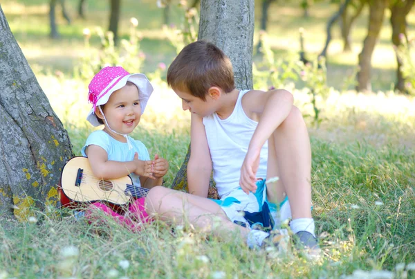 Chłopiec i jego młodsza siostra grać na gitarze i śpiewać w ogrodzie — Zdjęcie stockowe