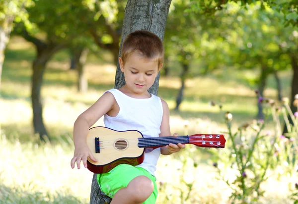 Liten pojke repeterar på sin akustiska gitarr — Stockfoto