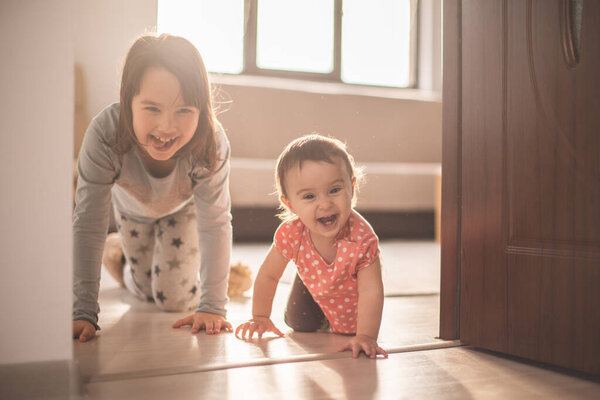 Девочка играет со своей младшей сестрой дома. Они веселятся, когда ходят на четвереньках.