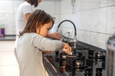 Küçük kız mutfakta annesinin yanında bulaşık yıkıyor.