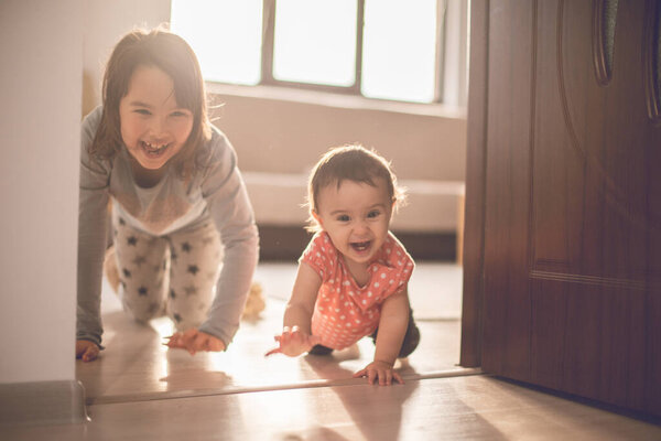 Девочка играет со своей младшей сестрой дома. Они веселятся, когда ходят на четвереньках.