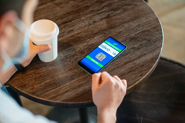 Man sitting at the table in the cafe thanks to the digital passport certifying that he was vaccinated