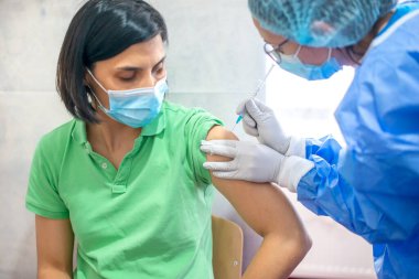 Aşı, aşı kampanyası, hastalık önleme konsepti. Tıbbi maske takan genç bir kadın doktordan Covid-19 aşısı alıyor. Profesyonel hemşire hastaya grip aşısı yapıyor.