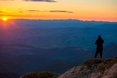 Dağın tepesindeki adam güneşin doğuşundaki güzel manzarayı fotoğraflıyor.