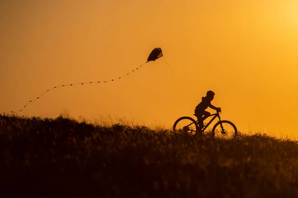 Silhouet Van Een Kind Fiets Met Een Vlieger Zijn Hand — Stockfoto