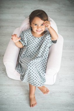 Küçük koltukta oturan ve kameraya gülümseyen tatlı küçük kız..