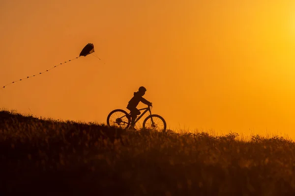 Silhueta Uma Criança Andando Bicicleta Com Papagaio Mão — Fotografia de Stock