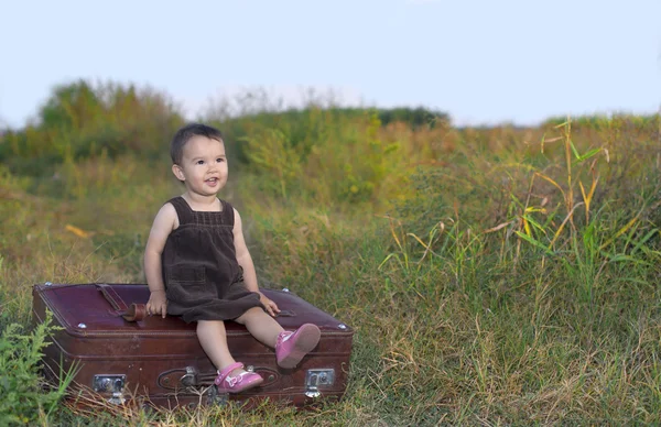 Malá dívka sedící na velký kufr — Stock fotografie