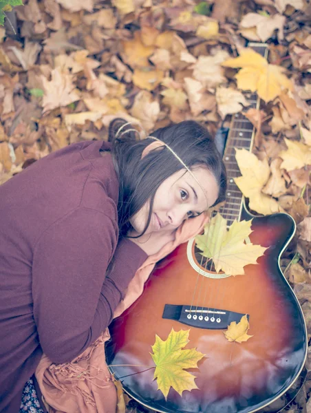 Hermosa chica descansando en hojas de otoño con guitarra — Foto de Stock