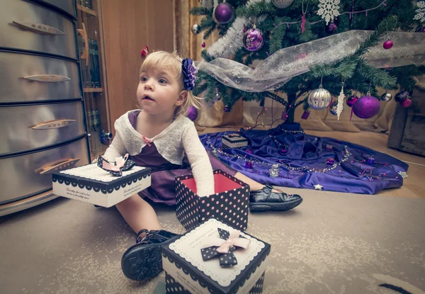 Blond meisje op zoek naar presenteert in de buurt van de kerstboom — Stockfoto