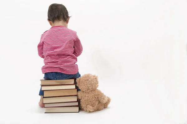 Verärgertes Kind sitzt mit Teddybär auf Büchern — Stockfoto