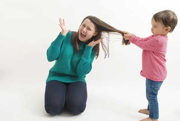 Una niña pequeña tira del pelo de su hermana mayor —  Fotos de Stock