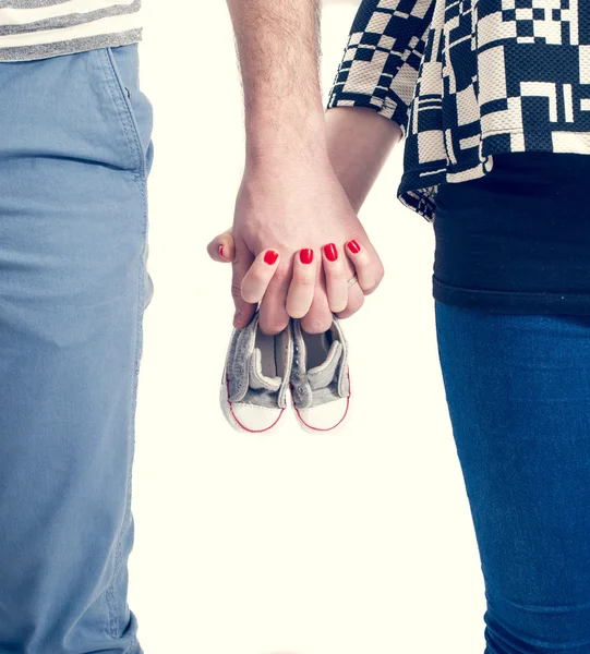 Futuros pais de mãos dadas e um par de pequenos sapatos sobre fundo branco — Fotografia de Stock