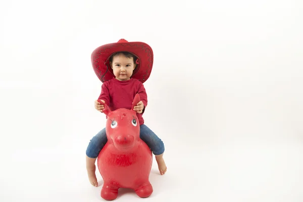 Menina com chapéu de cowboy vermelho equitação o brinquedo cavalo isolado — Fotografia de Stock