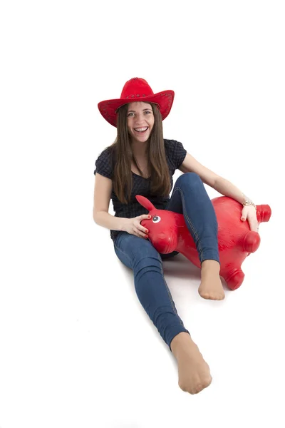 Young girl with red cowboy hat riding o toy horse isolated — Stock Photo, Image