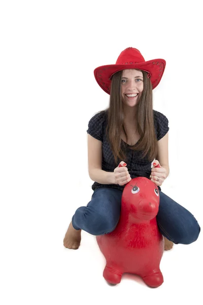 Young girl with red cowboy hat riding o toy horse isolated — Stock Photo, Image