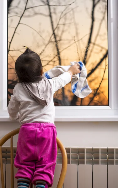 Kleines Mädchen reibt Glas mit Tuch am Fenster — Stockfoto