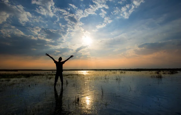 Mann, der bei Sonnenuntergang im Wasser die Arme in die Höhe reißt — Stockfoto