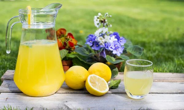 Limonade im Krug und Zitronen auf dem Tisch im Freien — Stockfoto