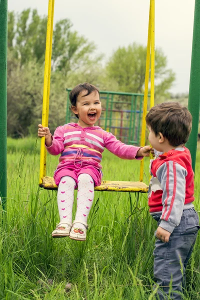 Двое маленьких детей веселятся на качелях в летний день — стоковое фото