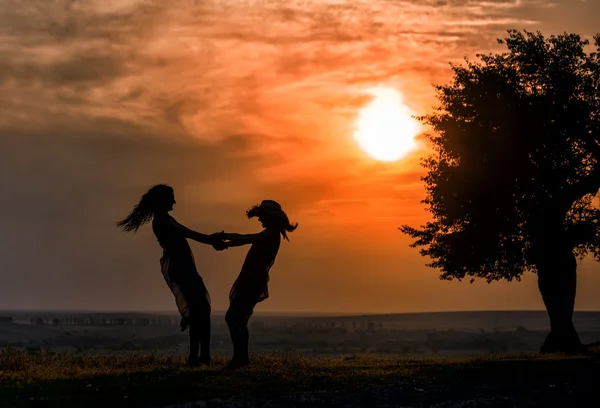 Una silueta de dos mujeres bailando sobre la hierba al atardecer — Foto de Stock