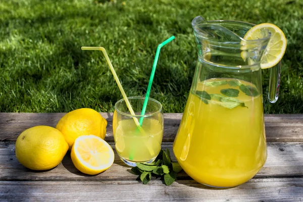 Limonata in brocca e limoni in tavola all'aperto — Foto Stock