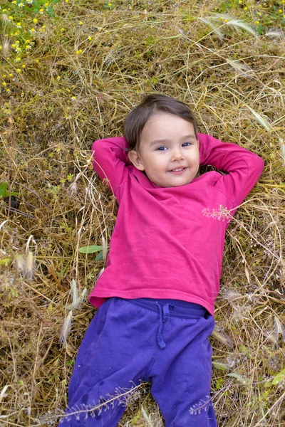 Portrait of a little girl smiling as she lies in  the grass — Stock Photo, Image