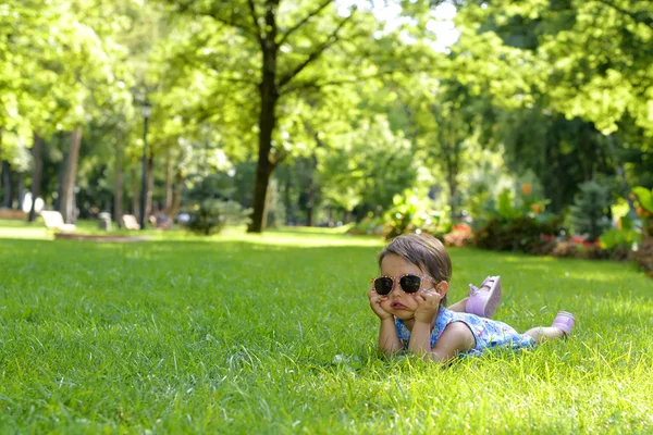 Linda niña pequeña tendida en la hierba en un día soleado de verano —  Fotos de Stock