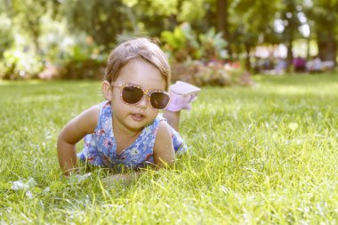 Bir güneşli yaz gününde çim döşeme gözlüklü şirin küçük kız