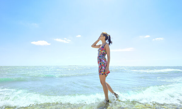 Young  woman standing in sea waves and holding her glasses
