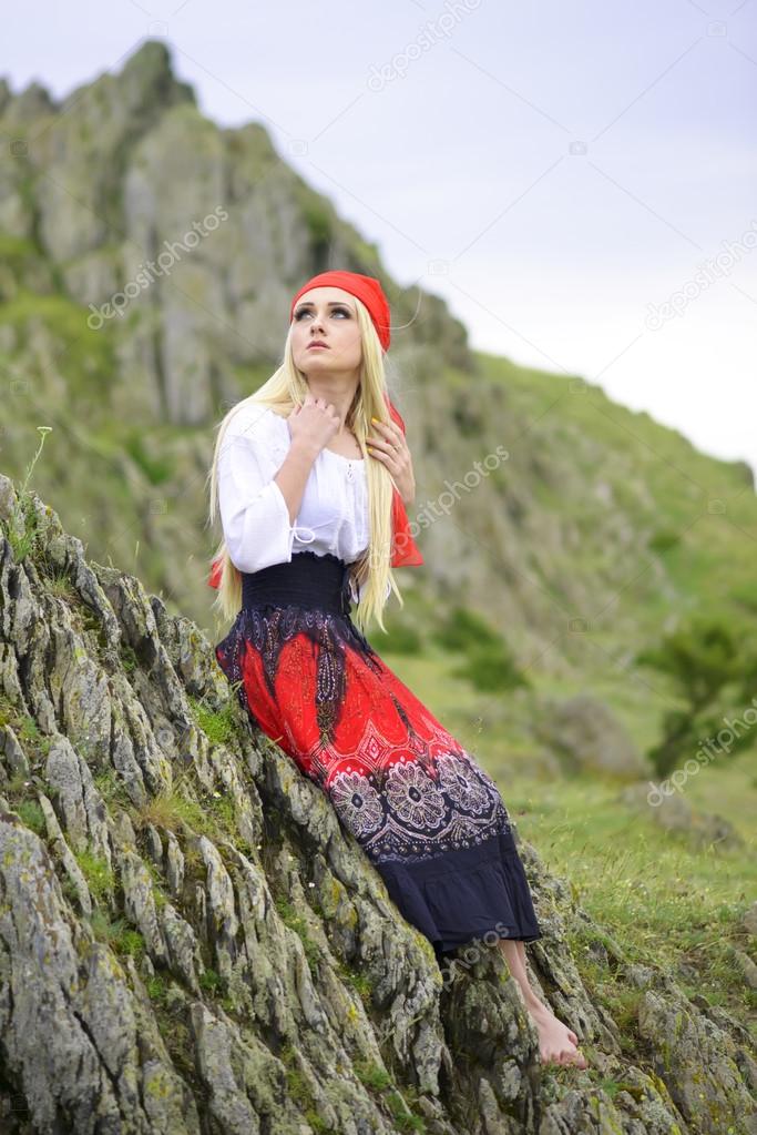 Beautiful blonde woman in old-fashioned dress sitting on a rock
