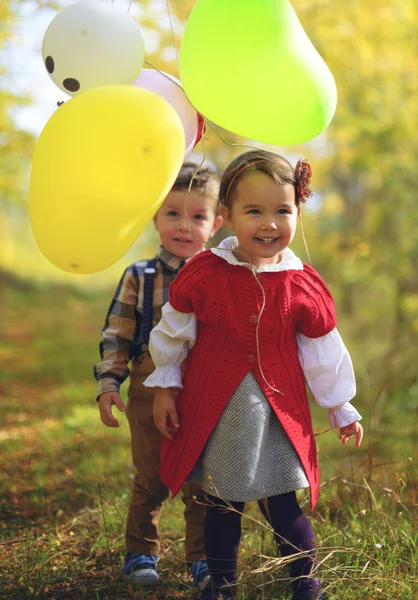Двое маленьких детей играют с воздушными шариками в парке осенью — стоковое фото