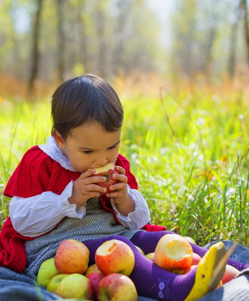 Kind mit roten Äpfeln sitzt auf Blättern im Herbstpark — Stockfoto