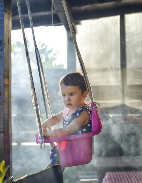 Маленькая девочка на качелях, окруженная дымом в саду — стоковое фото
