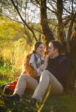 Genç çift oturma ve ormandaki ağaç yakınındaki gülüyor