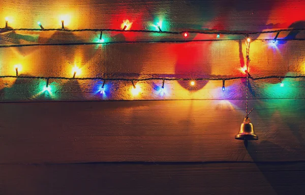 Рождественские огни и колокол на деревянном фоне — стоковое фото