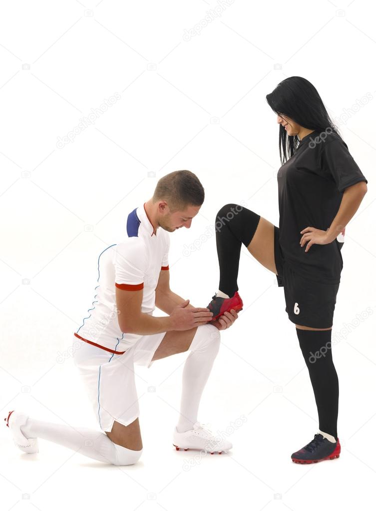 male soccer player cleaning female soccer player's shoe.  Man in white and woman in black;