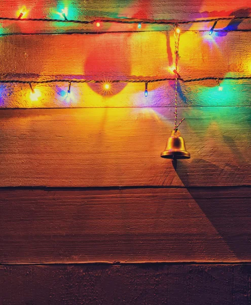 Kerstverlichting en bell op hout achtergrond — Stockfoto