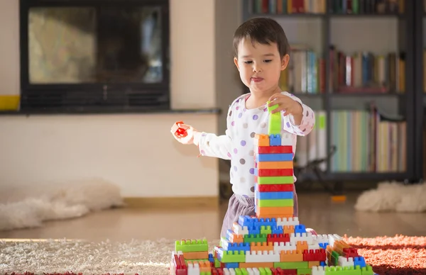 Brunett tjej i förskoleåldern leker med färgglada blocken sitter på ett golv — Stockfoto