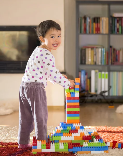 Brünettes Mädchen im Vorschulalter spielt mit bunten Blöcken, die auf einem Fußboden sitzen — Stockfoto