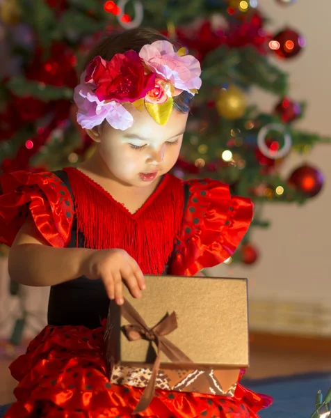 Little girl in red dress opens a present near the Christmas tree — Stock Photo, Image