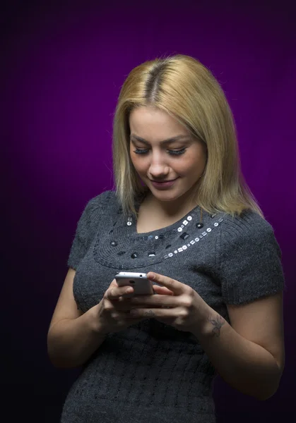 Konzentrierte blondhaarige Model hält Smartphone auf schwarzem Hintergrund — Stockfoto