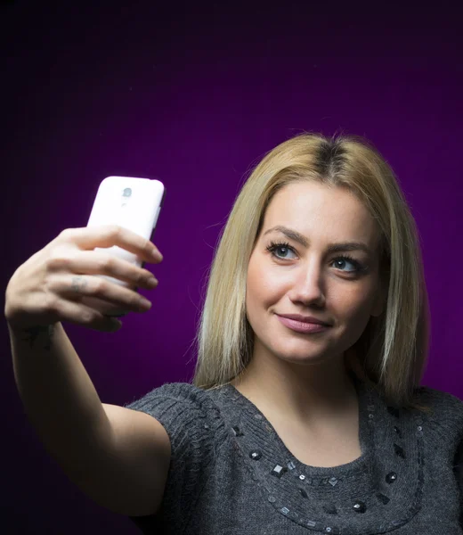 Glad blondin tjej med långt hår med selfie. Studio porträtt isolerad på lila bakgrund — Stockfoto